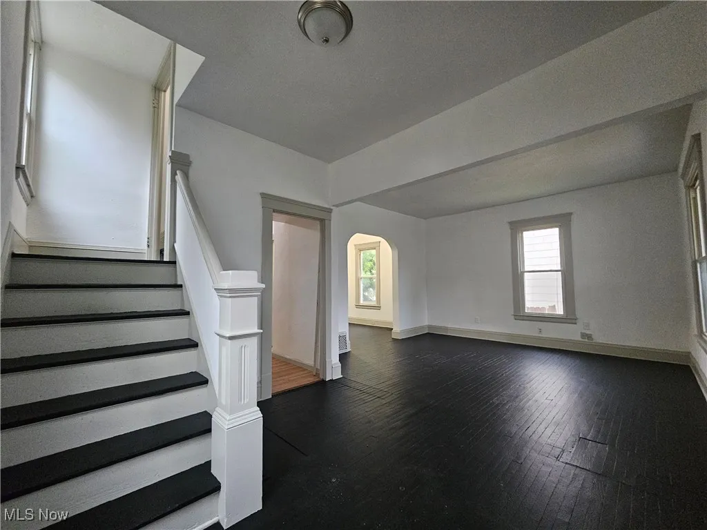 Unfurnished living room featuring arched walkways, stairway, and dark wood-type flooring