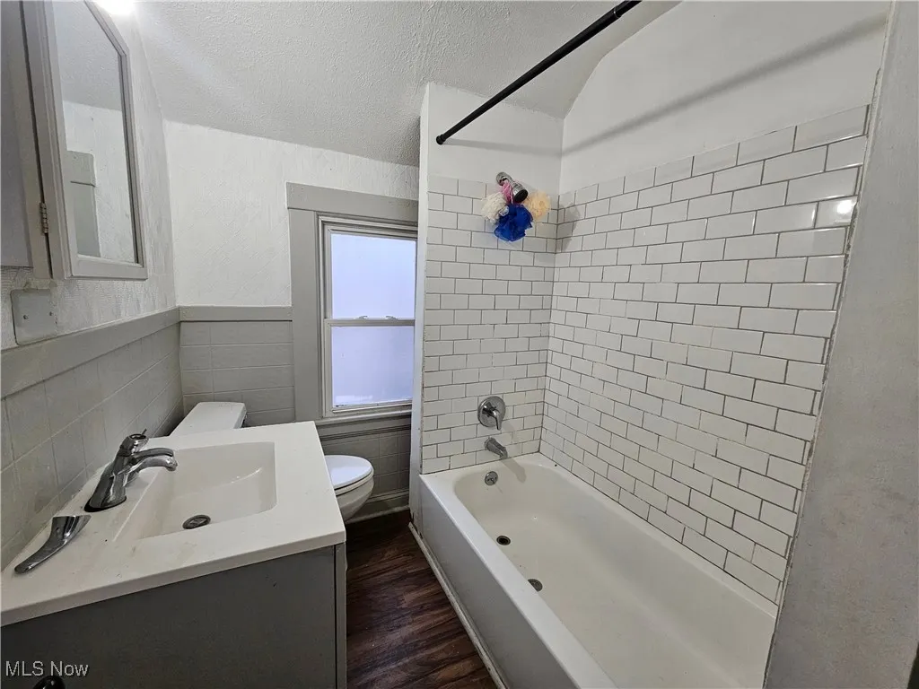 Full bathroom featuring washtub / shower combination, vanity, a textured ceiling, dark wood finished floors, and tile walls