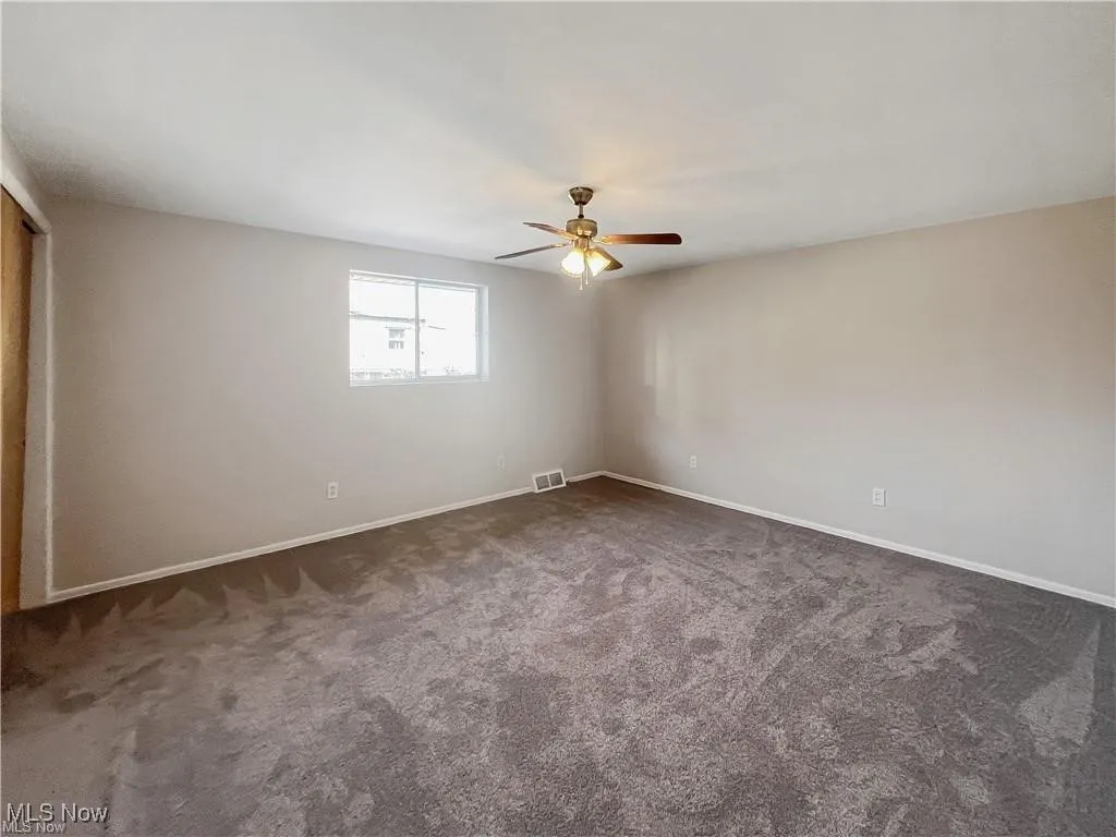 Unfurnished room with dark colored carpet and ceiling fan