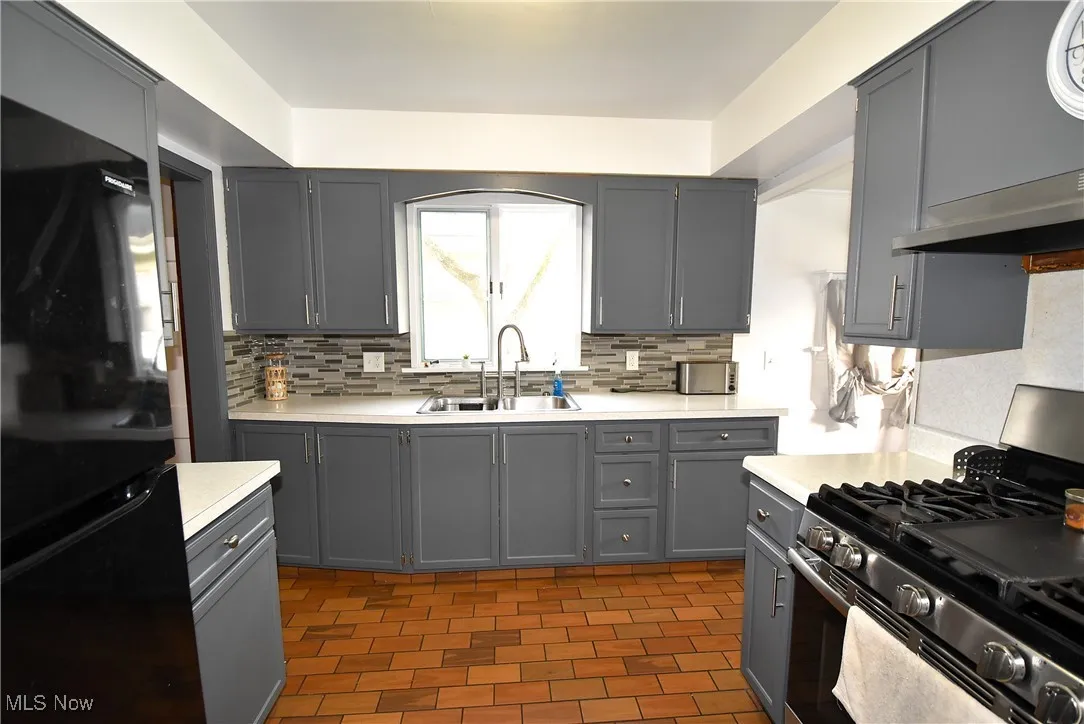 Kitchen featuring stainless steel range with gas cooktop, gray cabinets, freestanding refrigerator, and light countertops