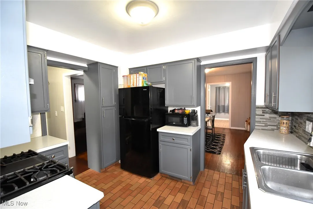 Kitchen featuring gray cabinets, black appliances, light countertops, and tasteful backsplash