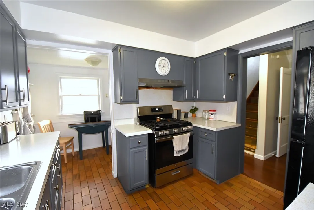 Kitchen featuring stainless steel range with gas stovetop, gray cabinets, freestanding refrigerator, light countertops, and brick patterned floors