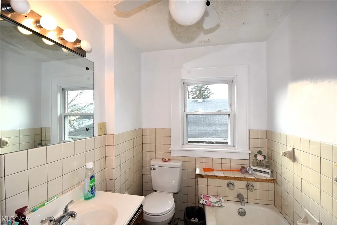 Full bath with a bath, vanity, plenty of natural light, tile walls, and wainscoting