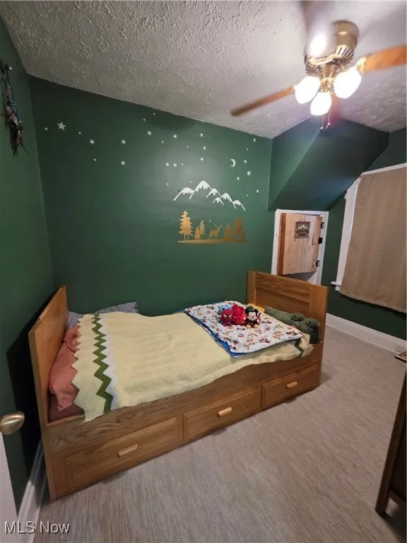 Carpeted bedroom featuring ceiling fan and a textured ceiling