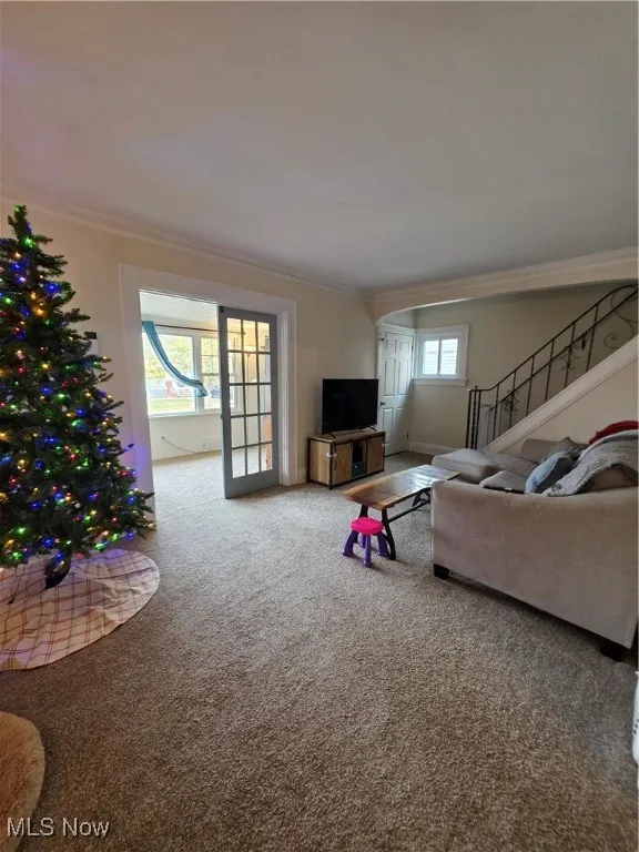 Living area with ornamental molding, stairs, carpet floors, and arched walkways