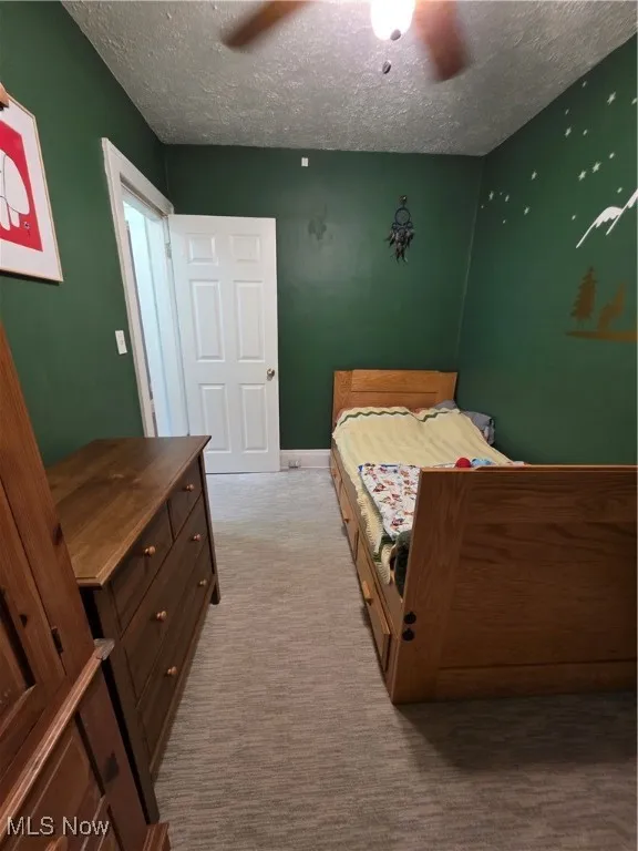 Carpeted bedroom featuring a ceiling fan and a textured ceiling
