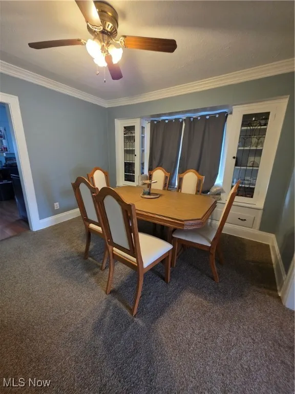 Dining area with ornamental molding, dark colored carpet, a ceiling fan, and a textured ceiling