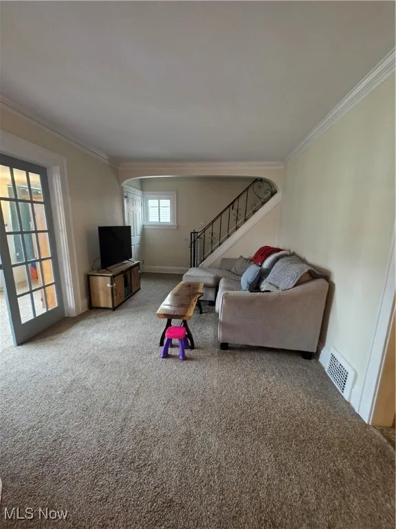 Living room featuring carpet floors, ornamental molding, stairs, and arched walkways