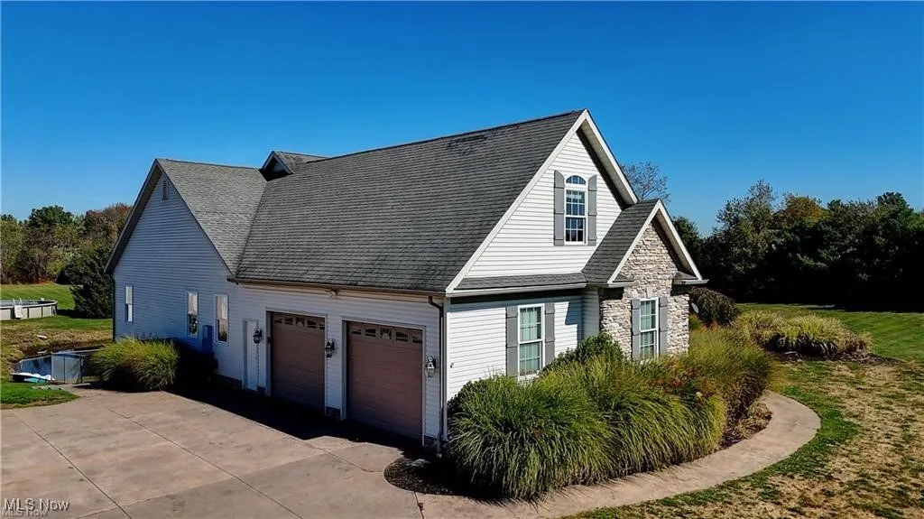 View of side of property with a shingled roof, driveway, and stone siding