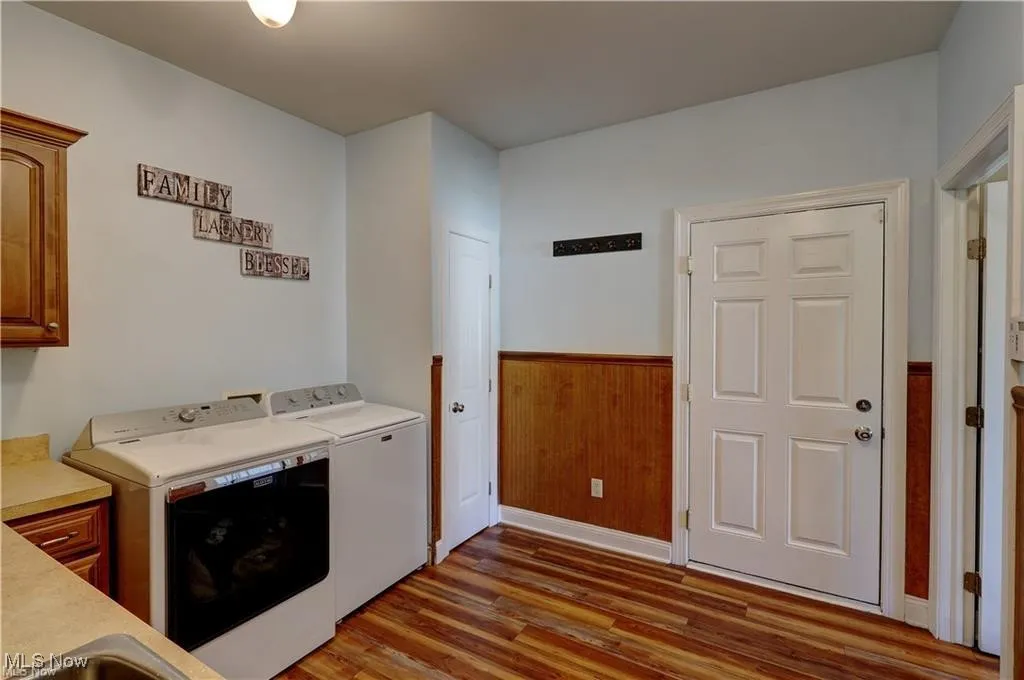 Laundry area with wainscoting, wooden walls, wood finished floors, and washing machine and clothes dryer
