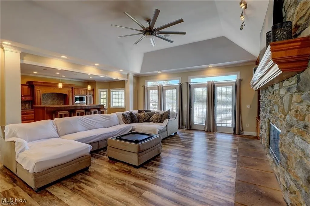 Living room with a fireplace, light wood-style floors, ceiling fan, and lofted ceiling