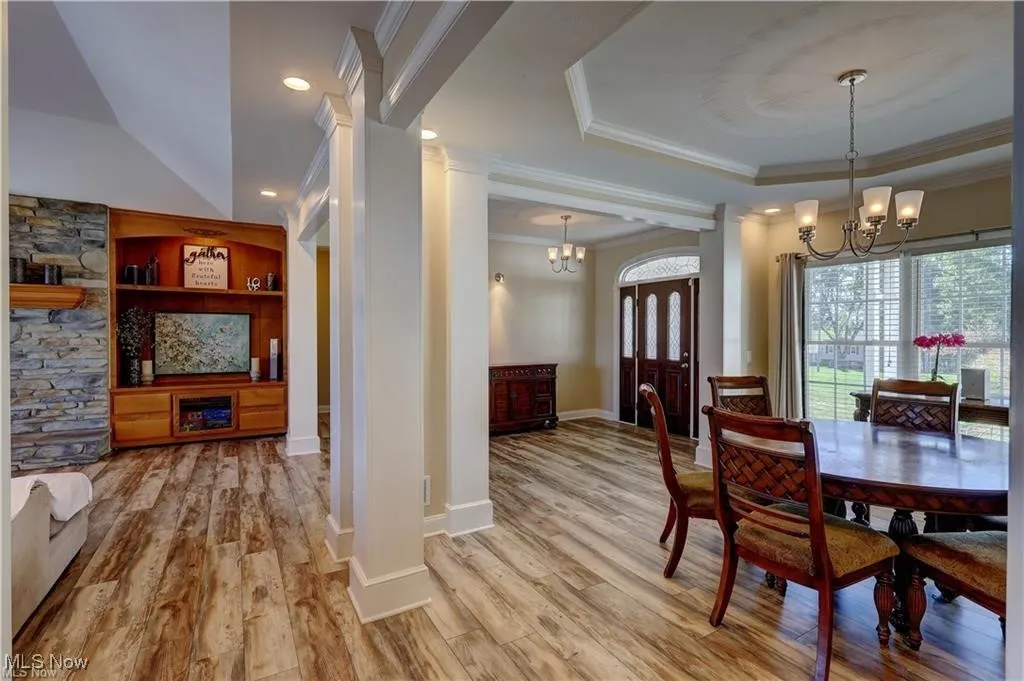Dining space featuring built in shelves, a chandelier, a raised ceiling, ornamental molding, and light wood finished floors