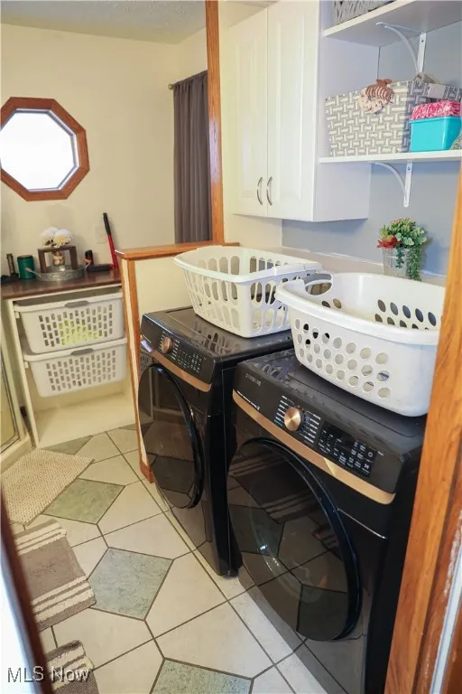 Washroom with cabinet space, washing machine and dryer, and light tile patterned floors