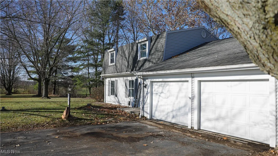 View of side of property featuring roof with shingles, a garage, a lawn, driveway, and a gambrel roof