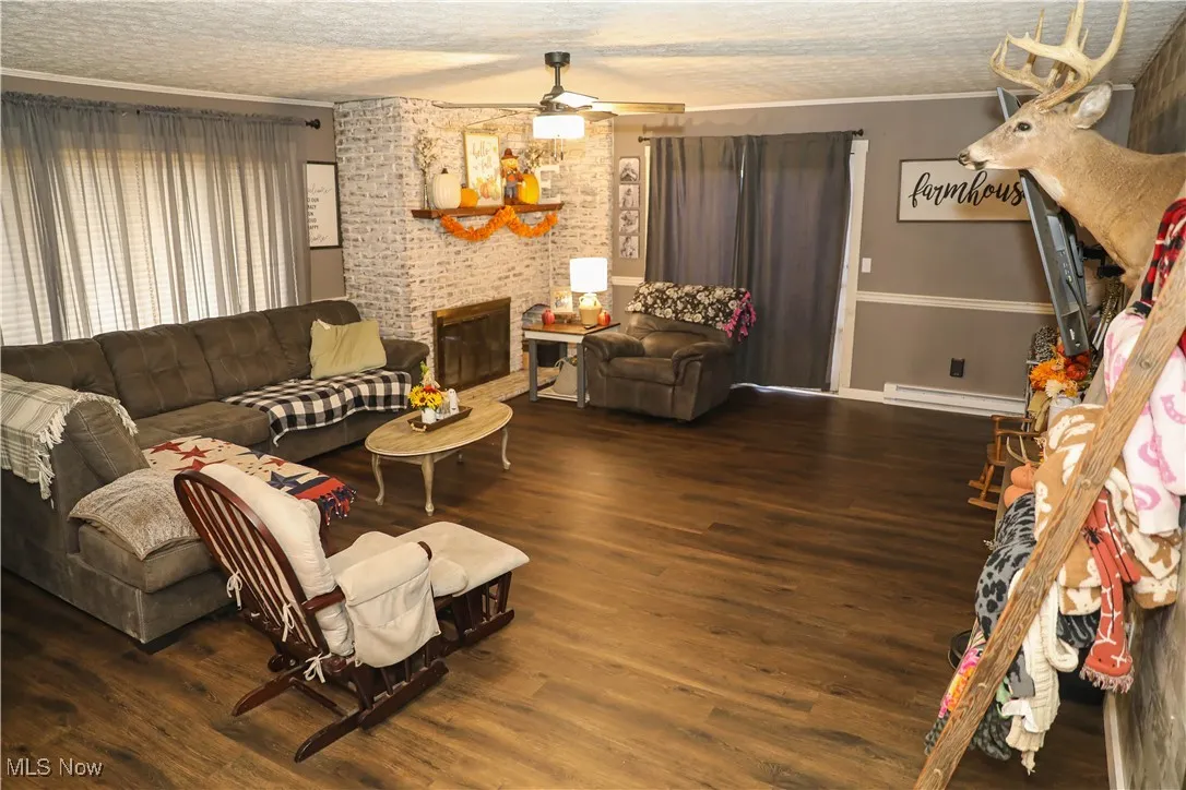 Living area featuring dark wood-style floors, a textured ceiling, baseboard heating, crown molding, and a brick fireplace