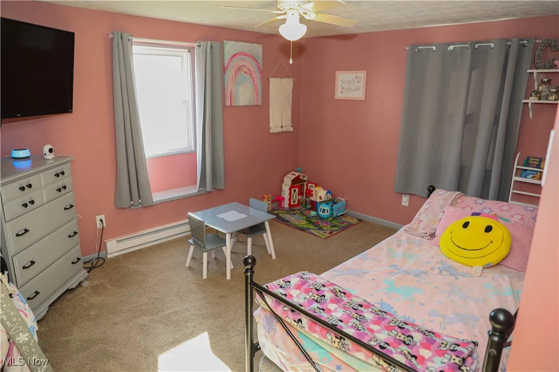 Bedroom featuring light colored carpet, baseboard heating, a ceiling fan, and a textured ceiling