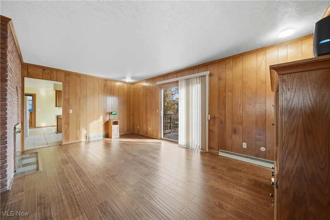 Unfurnished living room featuring wooden walls, wood finished floors, a textured ceiling, and a baseboard radiator