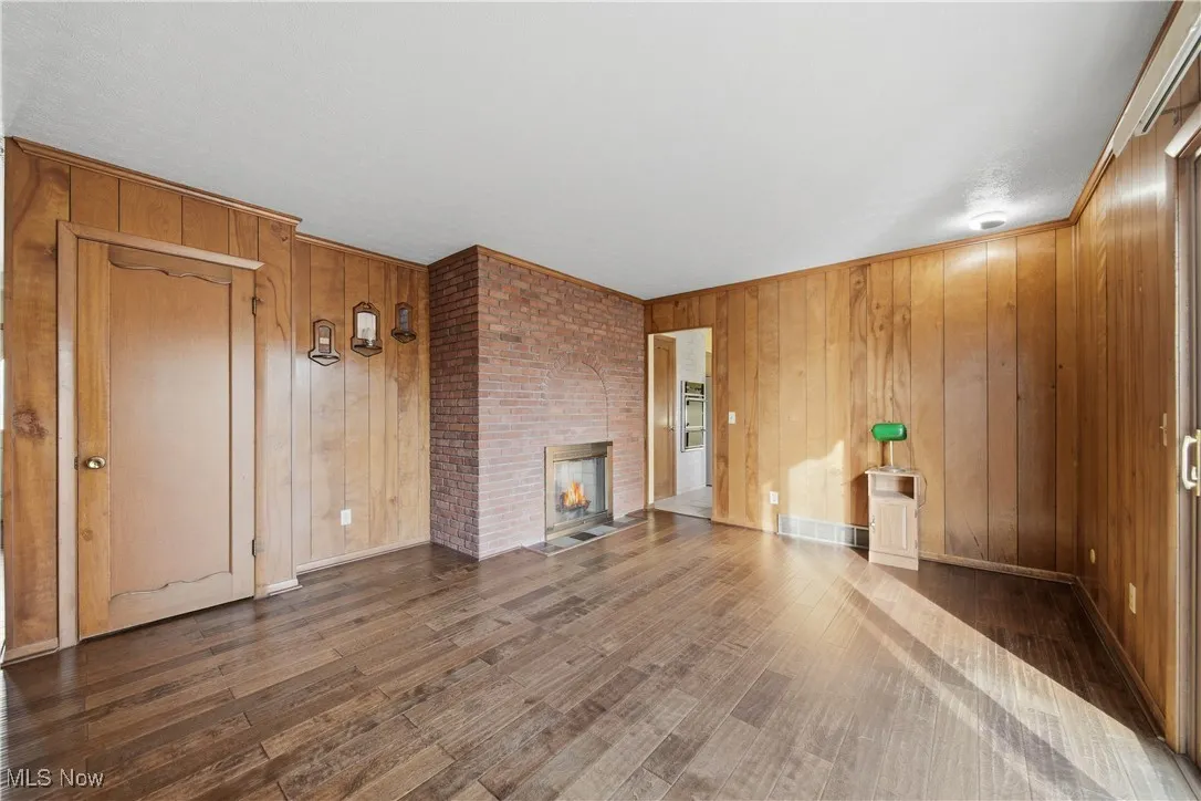 Unfurnished living room featuring a brick fireplace, wood walls, and dark wood finished floors