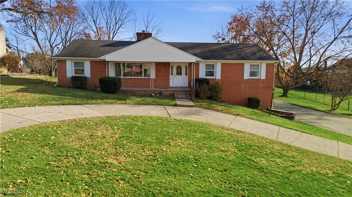 View of front facade with a front yard, brick siding, a chimney, and a porch