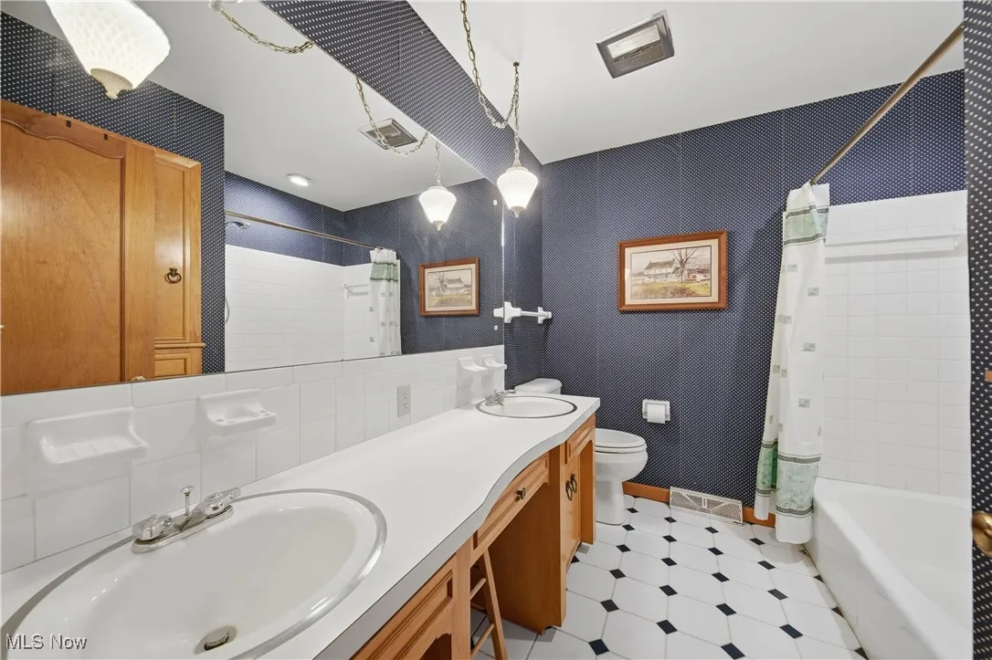 Full bath featuring double vanity, shower / bath combo with shower curtain, and light floors