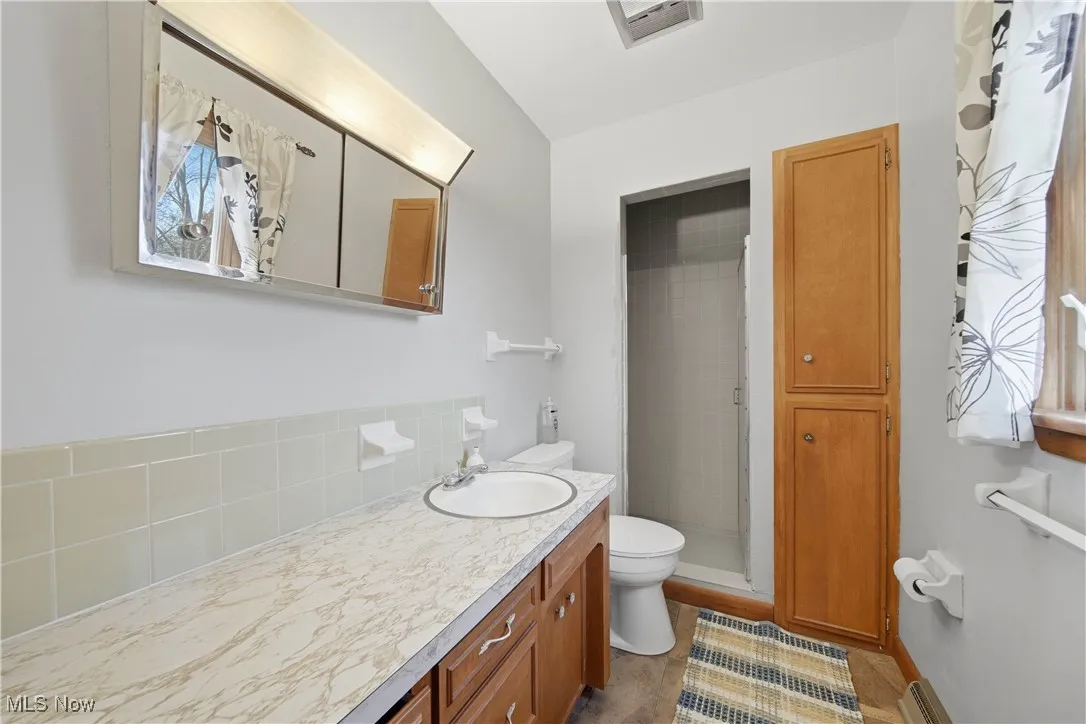 Full bathroom with a stall shower, vanity, backsplash, and a baseboard radiator