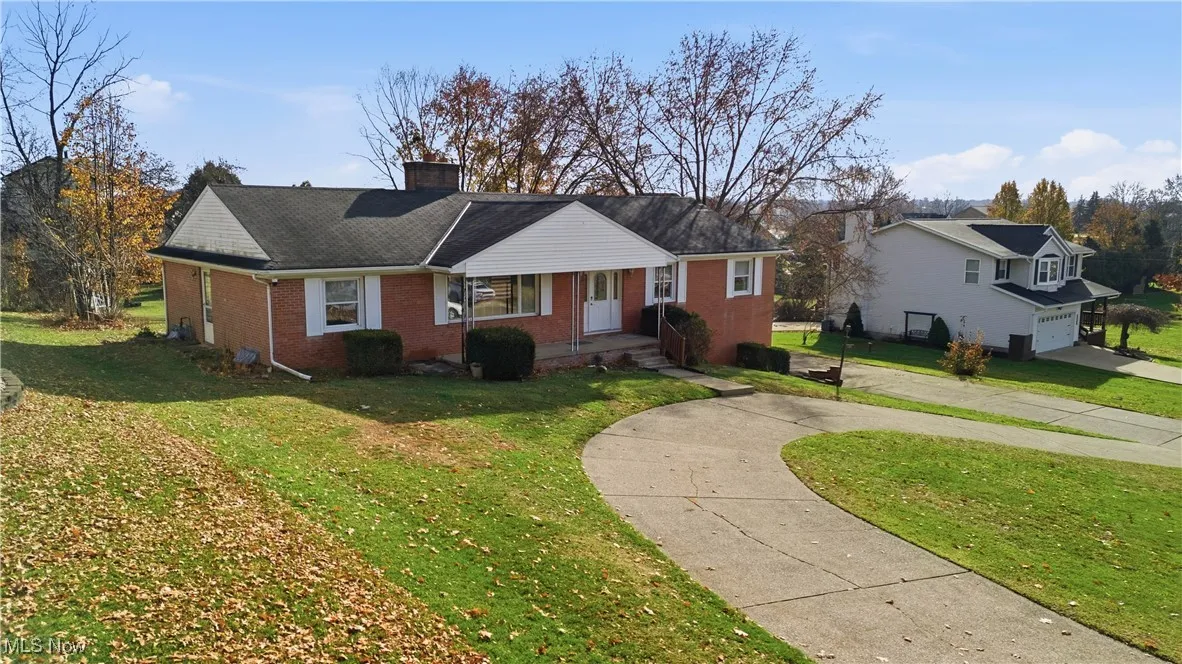 View of front of house featuring a front lawn, brick siding, a chimney, a shingled roof, and a garage