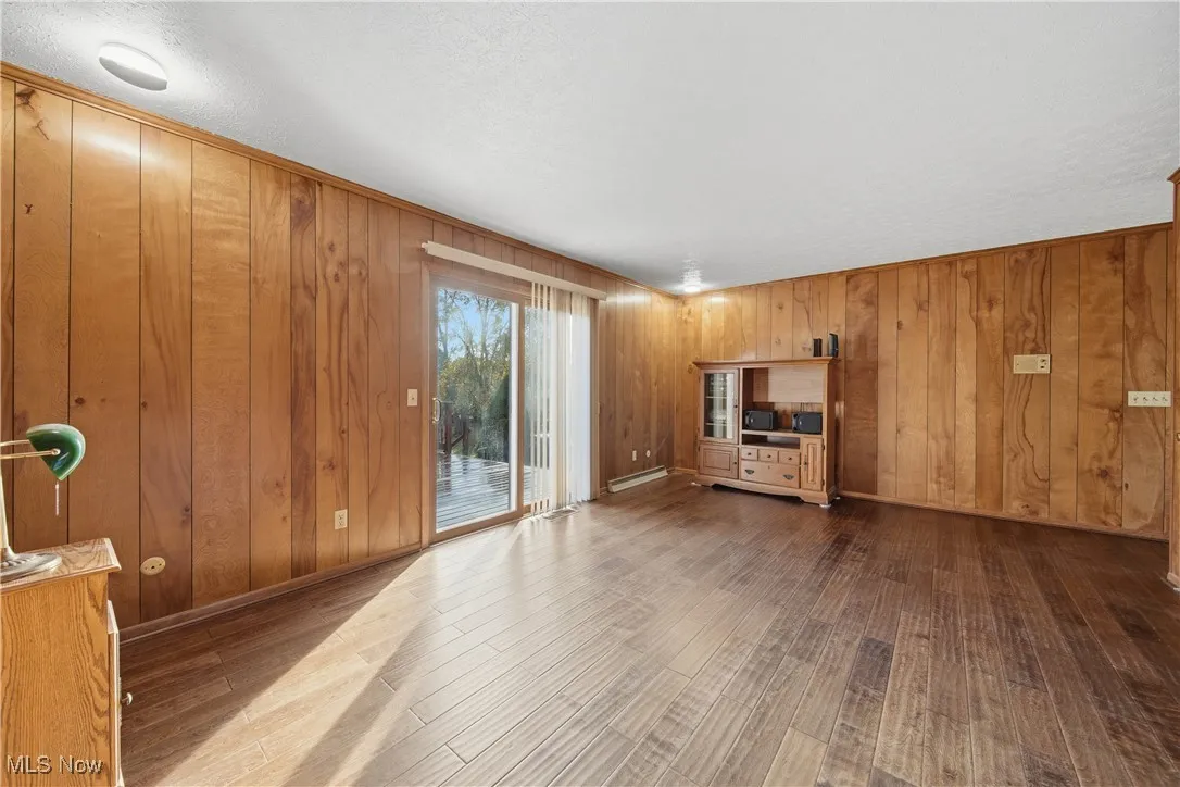 Unfurnished living room with wooden walls, wood finished floors, a textured ceiling, and a baseboard radiator
