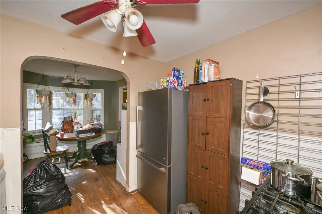 Kitchen featuring freestanding refrigerator, dark wood-style floors, arched walkways, brown cabinetry, and a ceiling fan