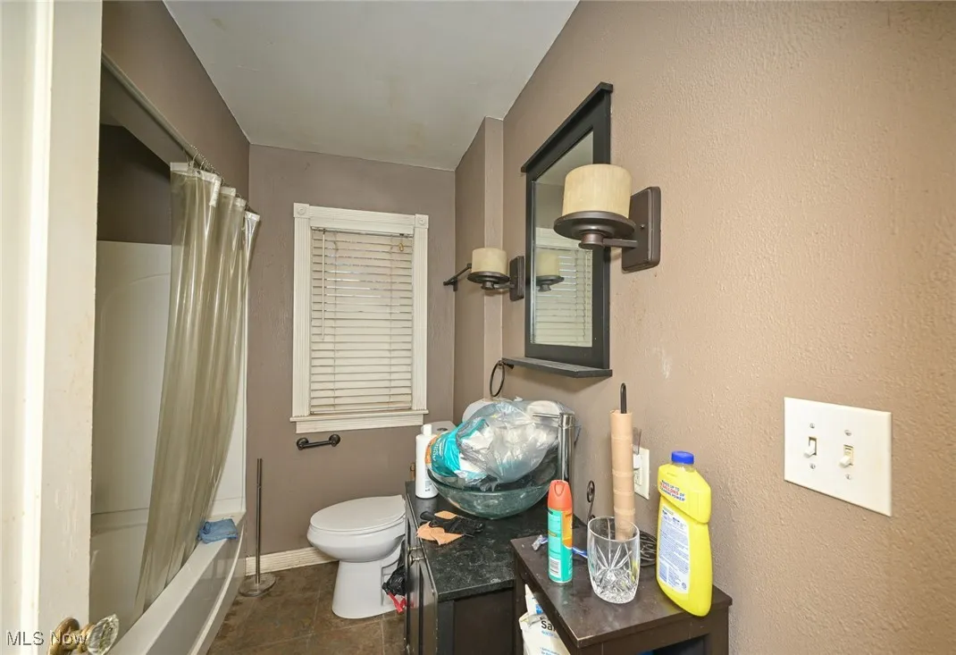Bathroom featuring shower / bath combination with curtain, vanity, dark tile patterned floors, and a textured wall