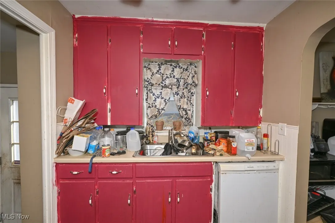 Kitchen featuring red cabinets, dishwasher, light countertops, arched walkways, and tasteful backsplash