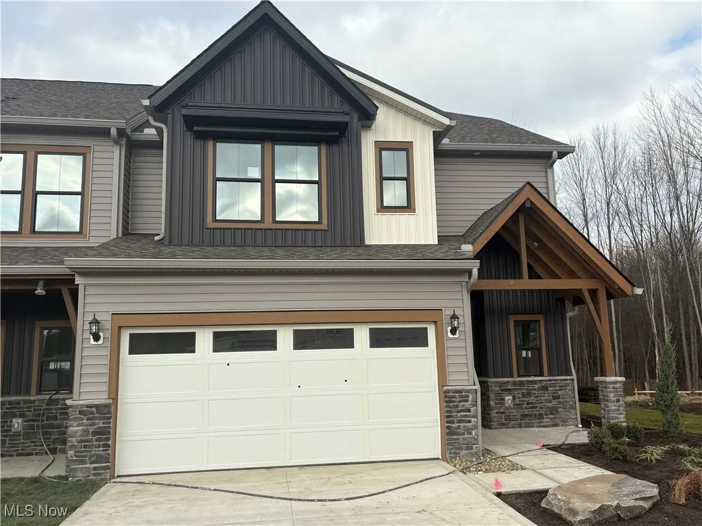 View of front of home with stone siding, a shingled roof, an attached garage, and concrete driveway