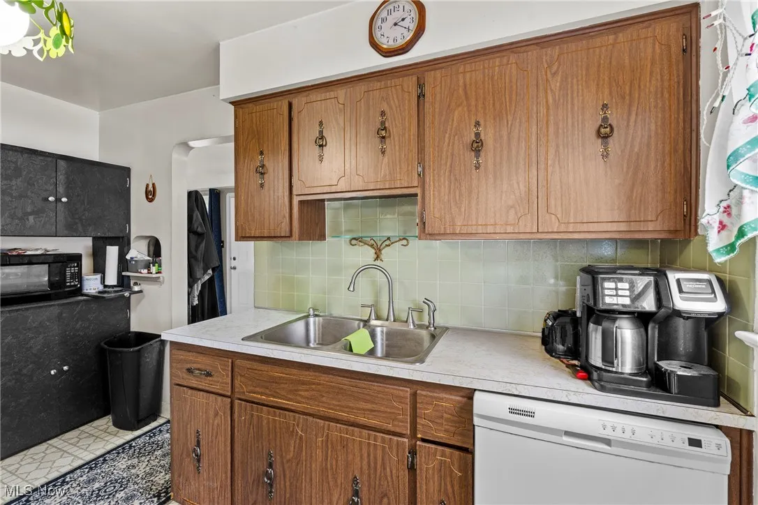 Kitchen featuring dishwasher, light countertops, brown cabinetry, and black microwave