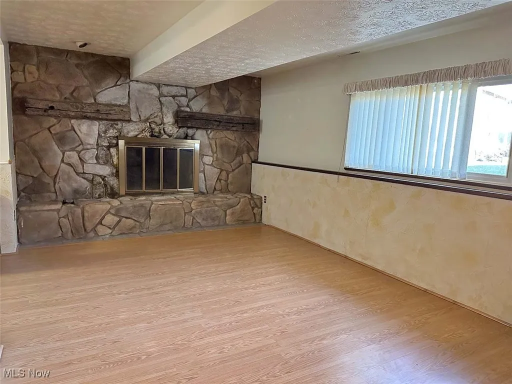 Unfurnished living room featuring a textured ceiling, a fireplace, and wood finished floors