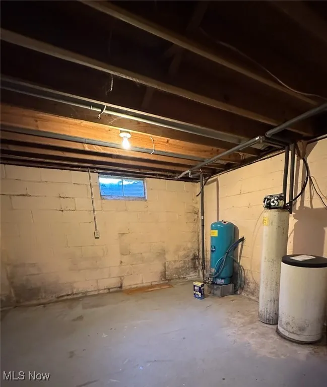Unfinished below grade area featuring a water softener system and a water pressure tank