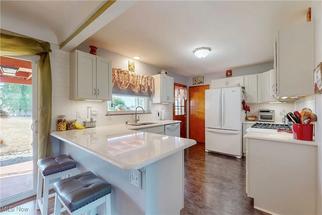 Kitchen with a peninsula, decorative backsplash, white appliances, a breakfast bar area, and white cabinetry
