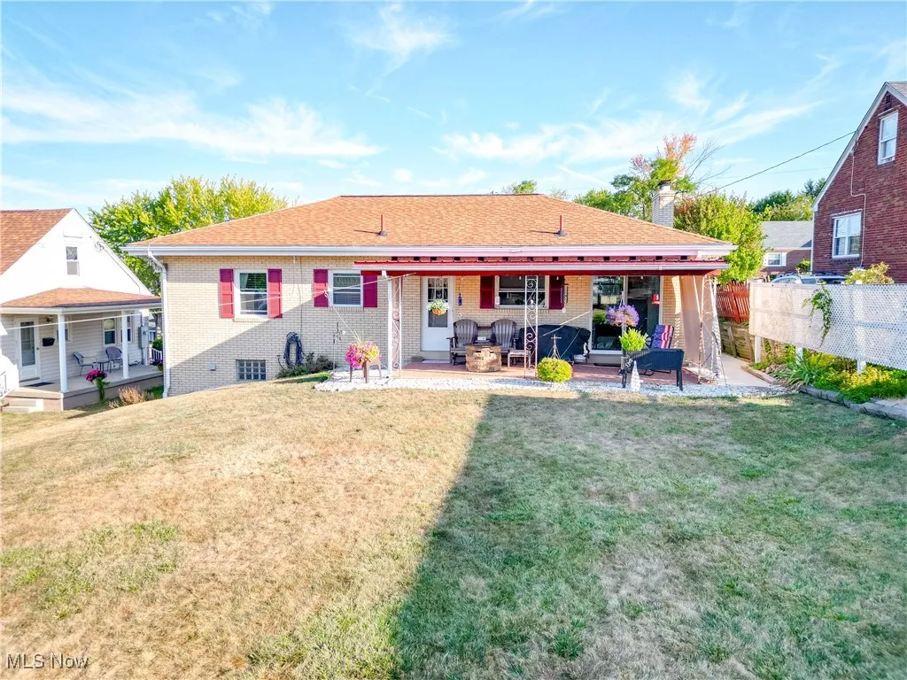 Back of property featuring a yard, brick siding, a patio, a chimney, and roof with shingles