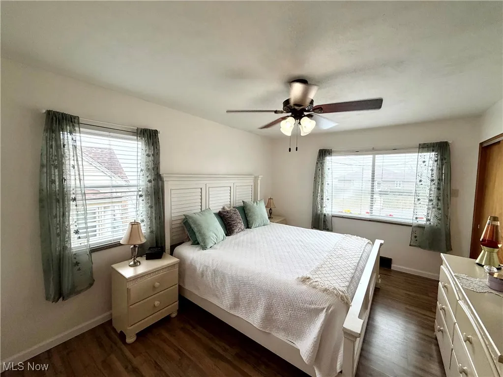 Bedroom with dark wood-type flooring, multiple windows, and ceiling fan