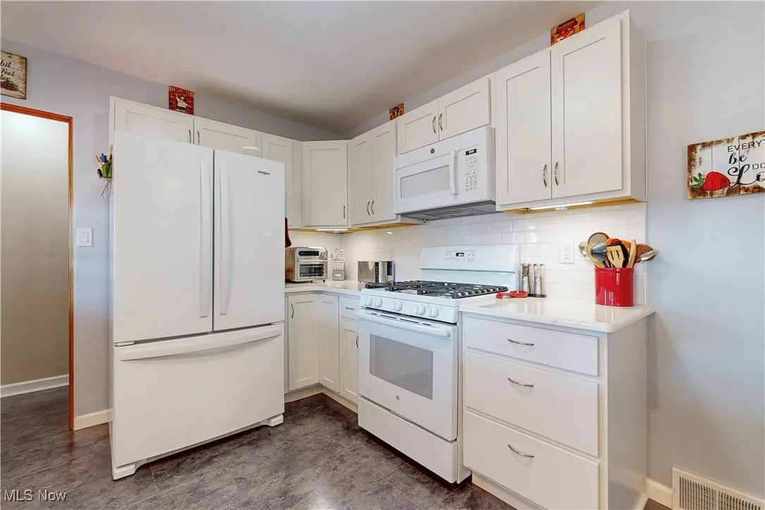 Kitchen with white appliances, white cabinetry, and tasteful backsplash