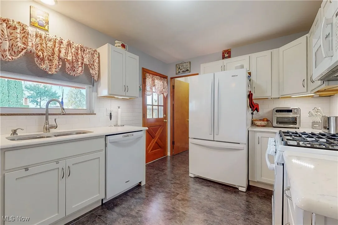 Kitchen featuring backsplash, white appliances, white cabinetry, and light stone countertops