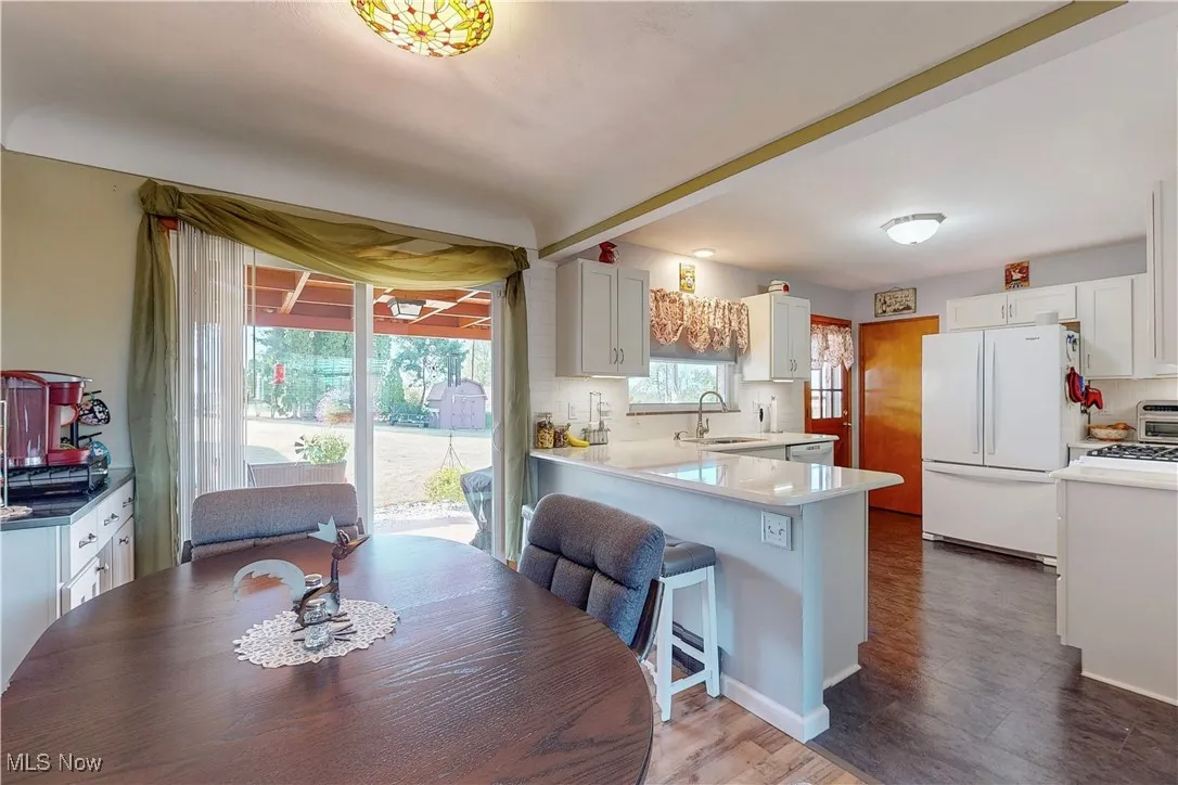 Kitchen featuring freestanding refrigerator, white cabinets, dark wood-style floors, a peninsula, and a kitchen bar