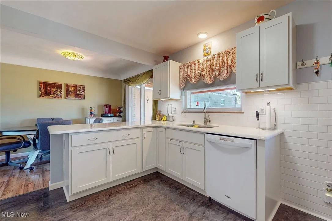 Kitchen featuring white dishwasher, a peninsula, white cabinetry, and tasteful backsplash
