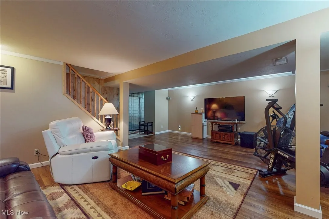 Living room with crown molding, wood finished floors, and stairway