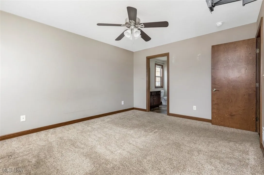 Unfurnished bedroom featuring carpet flooring, ensuite bathroom, and ceiling fan