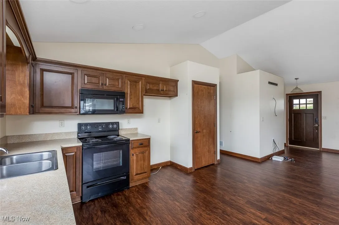 Kitchen with black appliances, light countertops, dark wood-type flooring, lofted ceiling, and brown cabinets