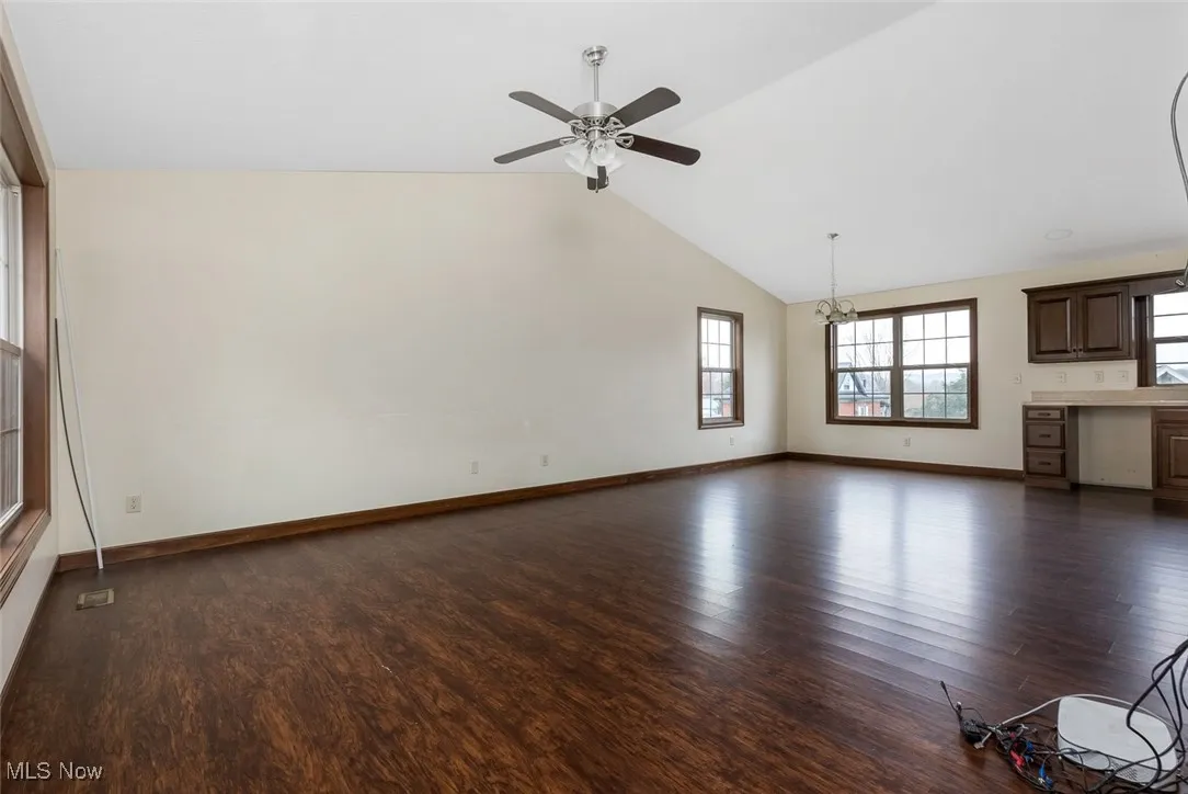Unfurnished living room featuring dark wood-type flooring, a ceiling fan, and high vaulted ceiling