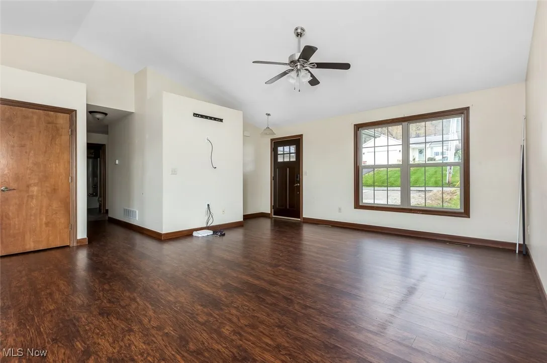 Unfurnished living room with vaulted ceiling, dark wood finished floors, and a ceiling fan