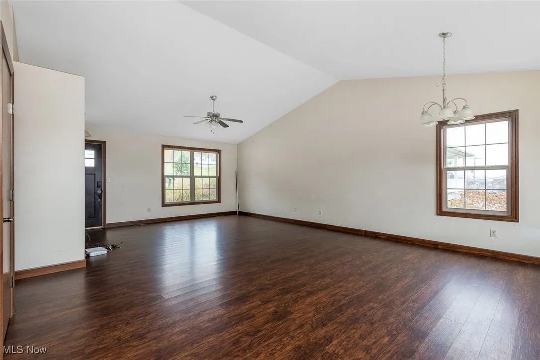 Unfurnished living room featuring dark wood-style flooring, lofted ceiling, a chandelier, and a ceiling fan