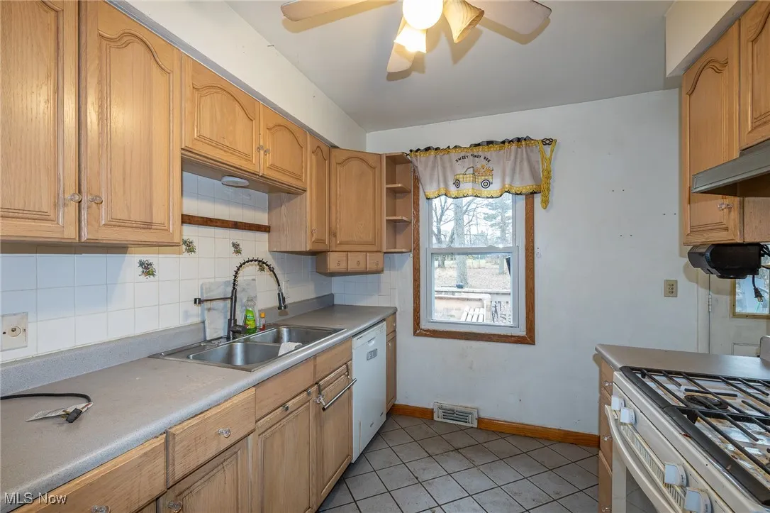 Kitchen with stainless steel gas range oven, light tile patterned floors, decorative backsplash, dishwasher, and open shelves