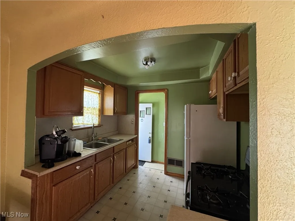 Kitchen with light floors, black appliances, brown cabinetry, light countertops, and arched walkways