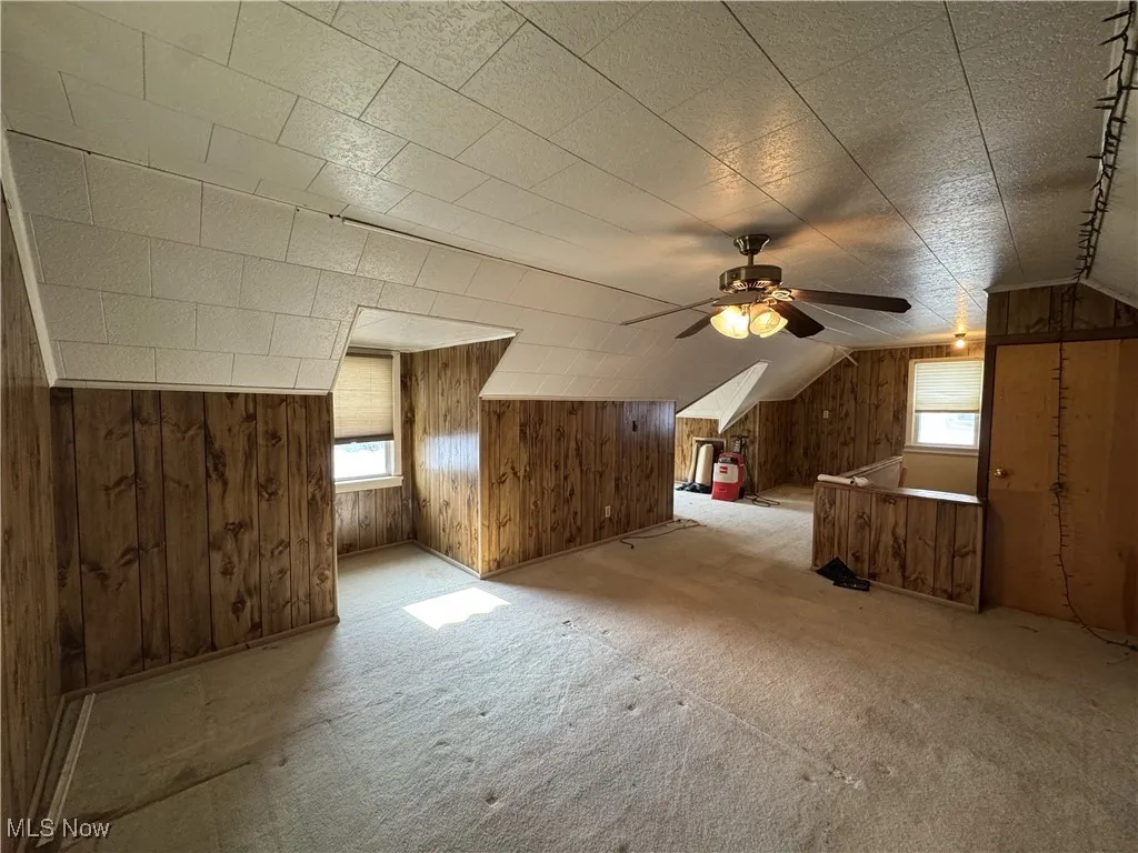 Additional living space featuring lofted ceiling, ceiling fan, wooden walls, and carpet floors